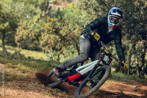 Unrecognizable man looking at camera in helmet, gloves and protection glasses jumping doing whip trick downhill during mountain biking practice in wood forest