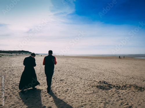 Fotografia Catholic priest in a cassock and a man walking on the beach in New Brighton, Eng