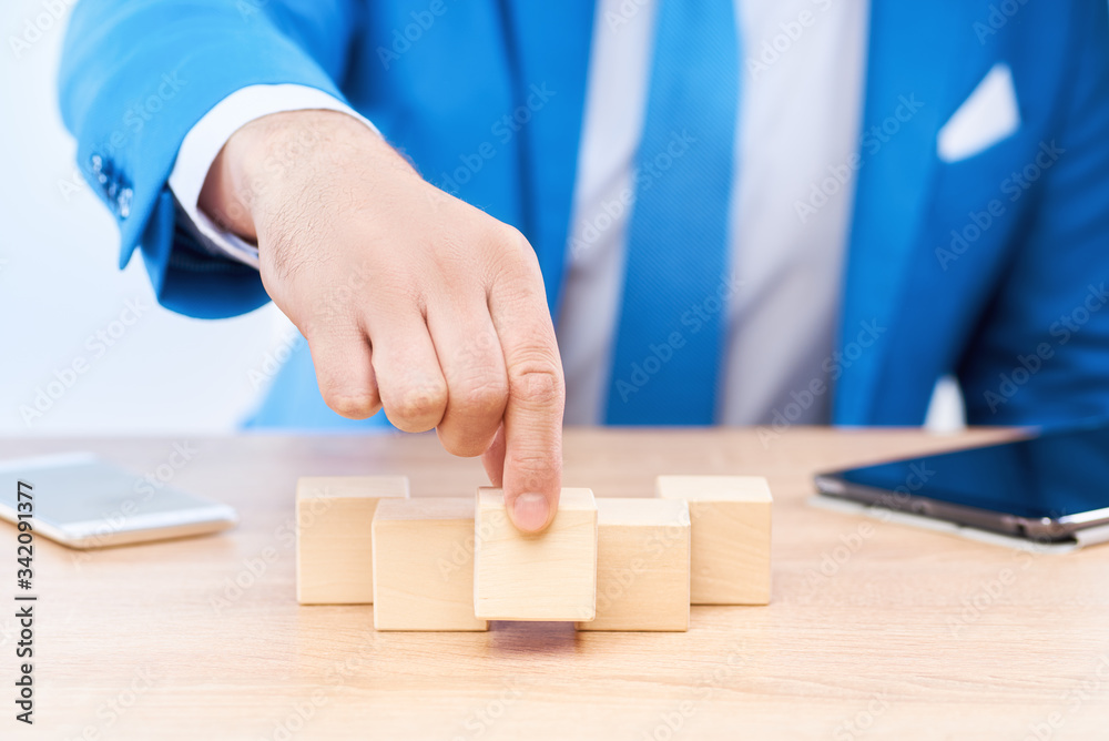 Six cubes lie in a pyramid on the businessman's table. The man holds the central cube in his hand. There is free space on the blocks for letters, numbers, symbols, or inscriptions. Six cubes lie in a pyramid on the businessman's table. The man holds the central cube in his hand. There is free space on the blocks for letters, numbers, symbols, or inscriptions.