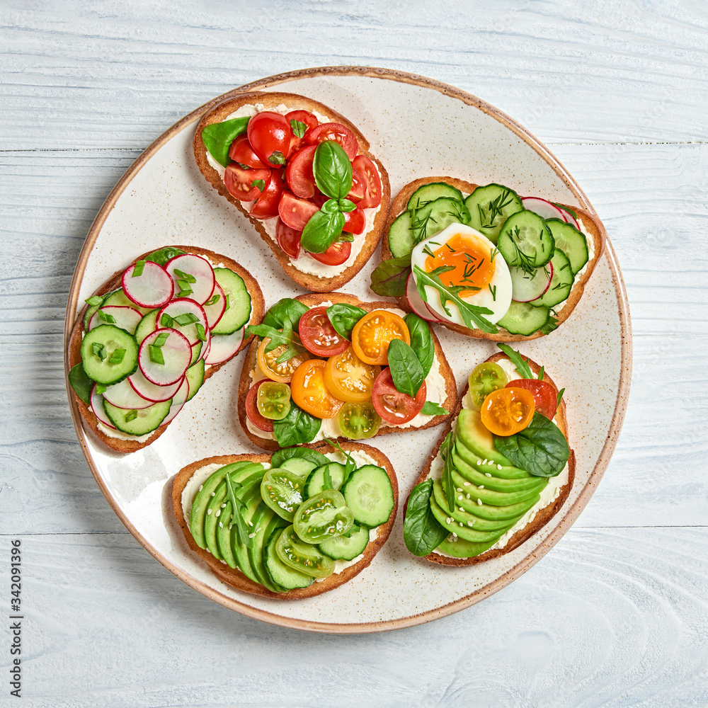 Italian vegan bruschetta on wooden background. Open sandwiches with avocado, cherry tomato, cucumber, radish. Various sandwich with spinach isolated on white, top view. Flat lay Italian vegan bruschetta on wooden background. Open sandwiches with avocado, cherry tomato, cucumber, radish. Various sandwich with spinach isolated on white, top view. Flat lay