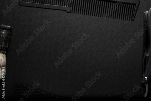 On a black surface are old hairdresser tools. combs, razor, shaving brush. black monochrome. horizontal orientation. top view. frame