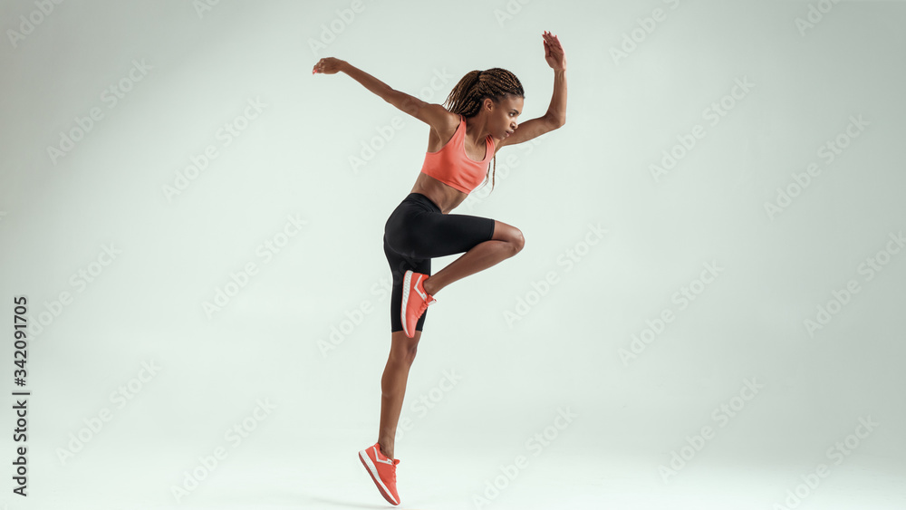 Never stop. Full length of young african woman with perfect body in sports clothing jumping in studio against grey background Never stop. Full length of young african woman with perfect body in sports clothing jumping in studio against grey background