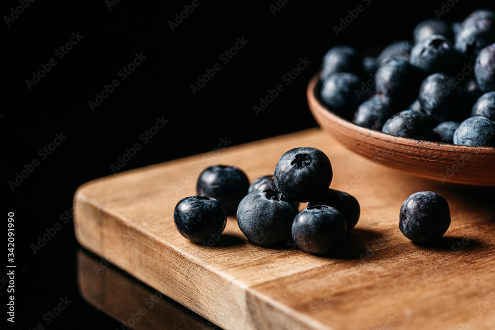 Fresh ripe blueberry placed on wooden table near bowl with berries against black background Fresh ripe blueberry placed on wooden table near bowl with berries against black background
