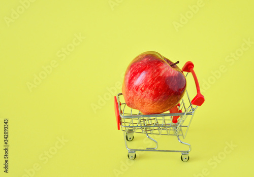 One fresh apple in Small shopping trolley closeup with on a yellow background. The concept of home delivery, online shopping, clearance sale.healthy food. food donatio photo