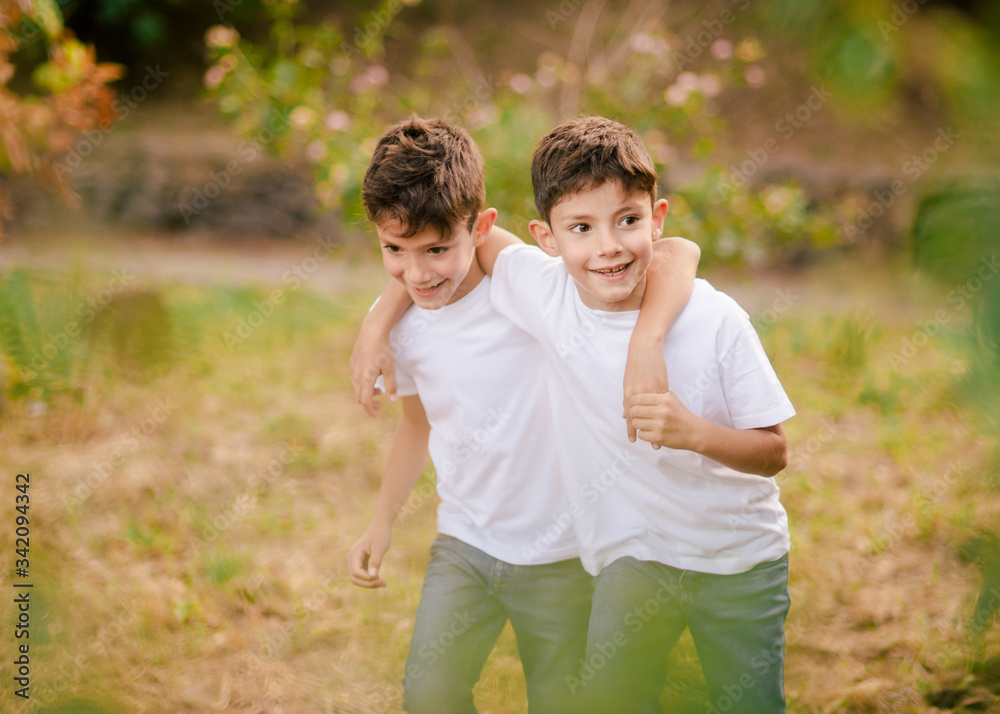 Happy twin boys hugging and looking away in park Happy twin boys hugging and looking away in park