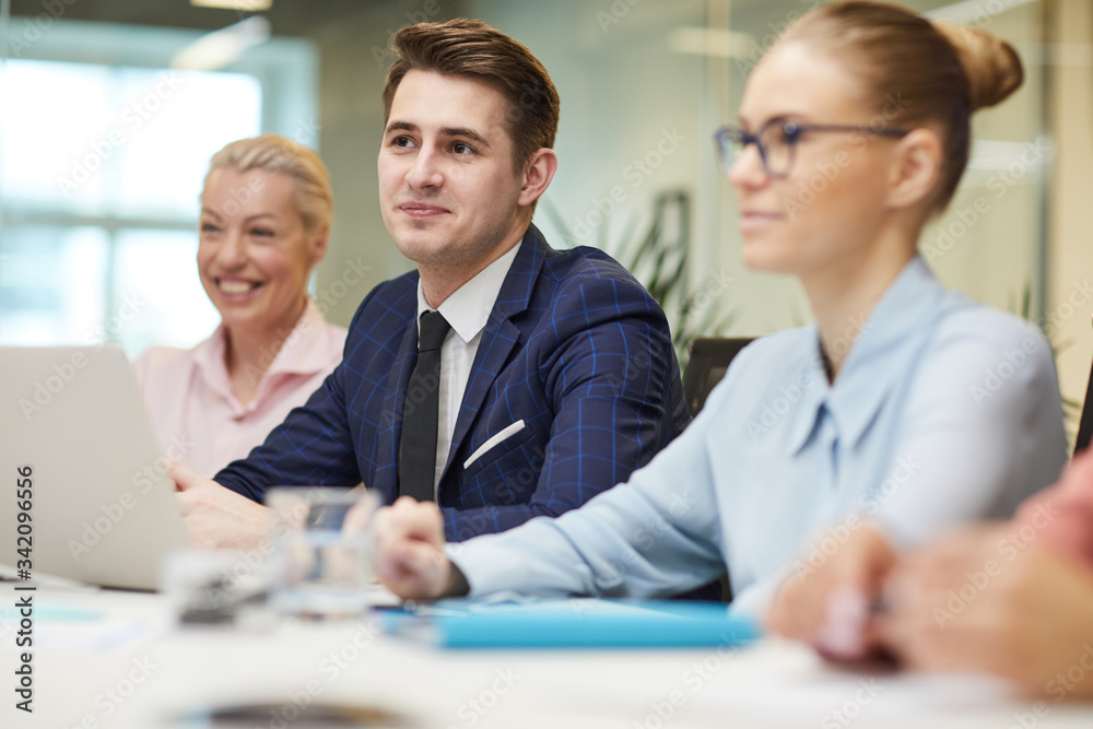 Young businessman in suit sitting at the table and listening to his colleagues during teamwork at meeting at office Young businessman in suit sitting at the table and listening to his colleagues during teamwork at meeting at office