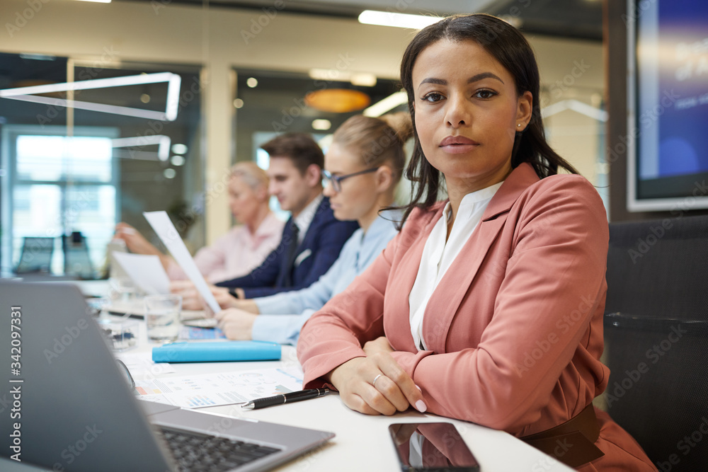 Portrait of young African businesswoman sitting at the table in front of laptop and looking at camera during business meeting at office