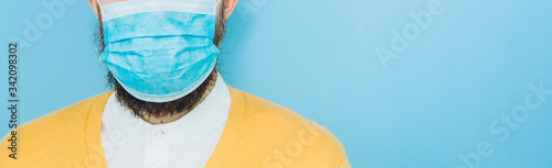 A young man in a medical mask on a blue background. A man in a yellow cardigan shows a hand gesture OK. We re going to beat coronavirus. The COVID-2019 epidemic. Positive boy.