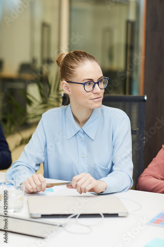 Young businesswoman in eyeglasses sitting at the table and listening to the speaker at meeting at office © AnnaStills