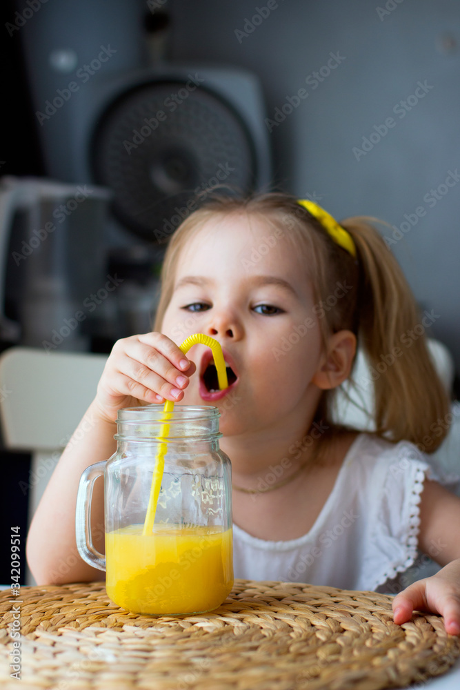 Little girl drinks fresh orange juice from a glass cup in the kitchen Little girl drinks fresh orange juice from a glass cup in the kitchen
