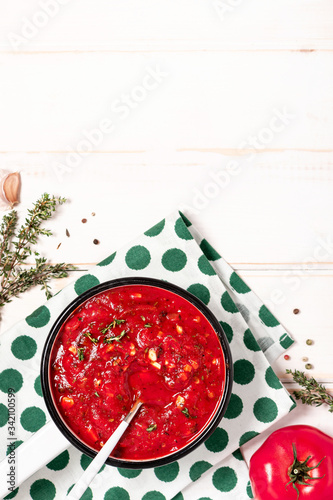 Homemade tomato sauce with herbs and garlic in a white pan on a white wooden table, top view, copy space. Bowl with homemade ketchup, tomatoes and herbs on a white background, free space for text