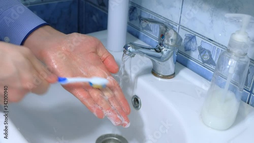 Man is washing hands with antibacterial soap and toothbrush against coronavirus in sink, hands closeup. Infection covid-19 pandemic. Hygienic procedures at home. Obsessive compulsive disorder symptom. photo