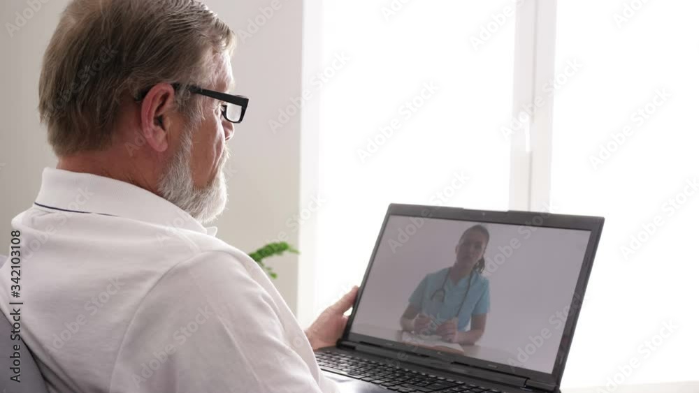 Online doctor. An elderly man sits with a laptop on the couch in his apartment, consults a doctor via the Internet. Online doctor. An elderly man sits with a laptop on the couch in his apartment, consults a doctor via the Internet.