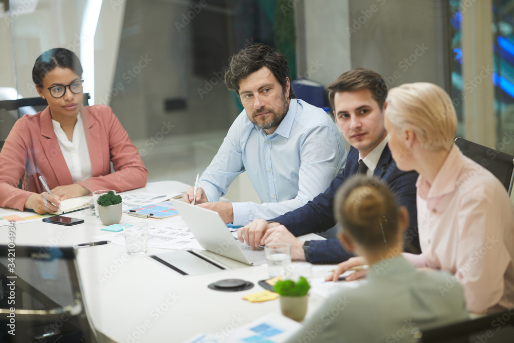 Group of colleagues sitting at the table talking to each other and planning work together at meeting at office