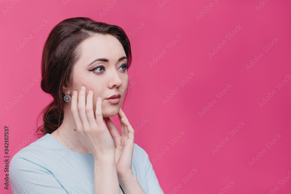 Beautiful girl shakes her face with her hands on a pink background in the studio. The concept of skin care. Beautiful girl shakes her face with her hands on a pink background in the studio. The concept of skin care.