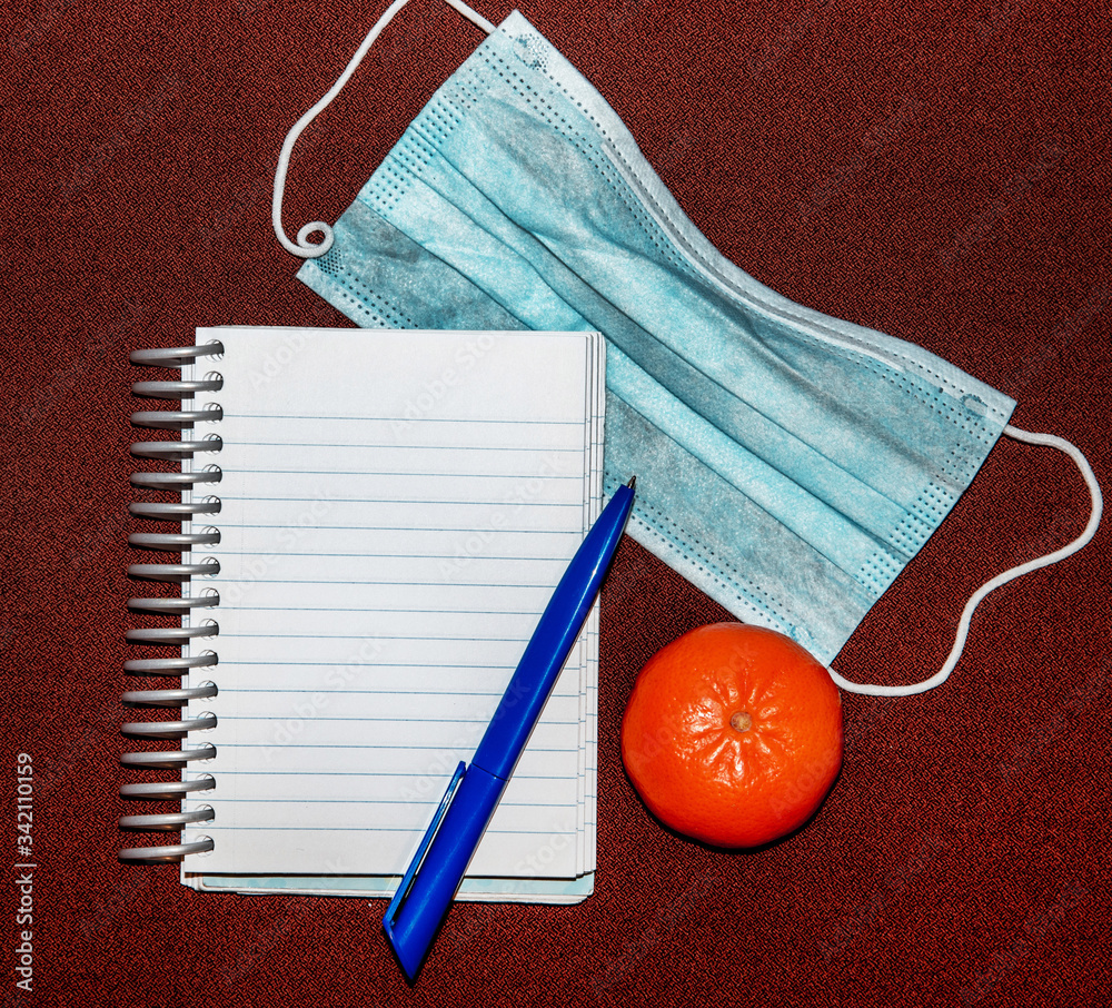 Abstract image with medical mask, tangerine, pen and notepad with blank lettering.