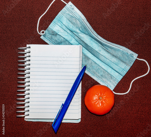 Obraz na płótnie Abstract image with medical mask, tangerine, pen and notepad with blank lettering. w salonie
