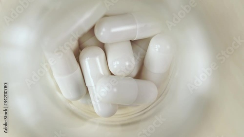 Medicinal white capsules in a glass bottle close-up on a wooden table. Macro shot. Slow rotation. View from above. Coronavirus treatment. The use of vaccines from Covid-19. photo