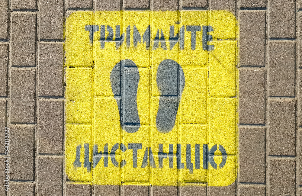 Fototapeta premium Yellow sidewalk with the warning Keep your distance on the sidewalk. The text is in Ukrainian. Concept of maintaining social distance, quarantine or isolation.