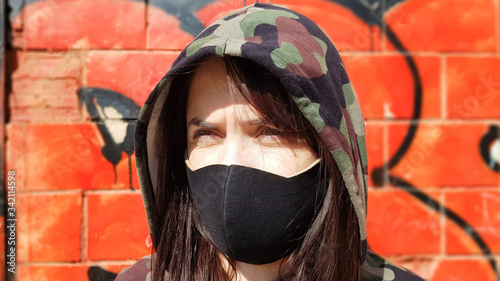 Portrait of a woman in a protective black mask outdoors near an old broken wall. Coronavirus and air pollution concept. A girl wears a protective mask to protect against a pandemic.