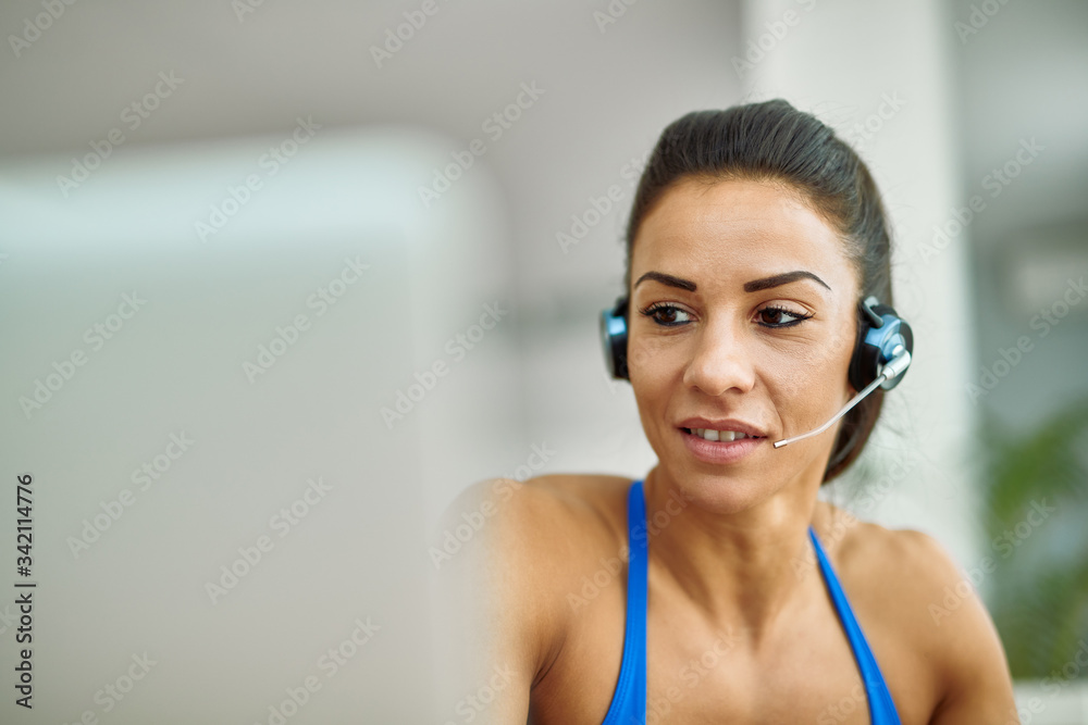 Naklejka premium Young sportswoman with headset using computer at home.