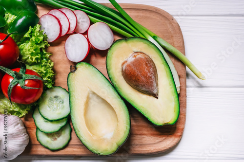 Fresh avocado with vegetables on cutting board over wooden backg