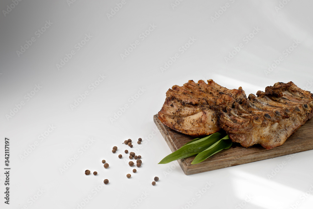 the ribs baked in the oven are placed on a wooden Board with ramson and allspice. baked meat for the holiday table. barbecue ribs for restaurant menu the ribs baked in the oven are placed on a wooden Board with ramson and allspice. baked meat for the holiday table. barbecue ribs for restaurant menu