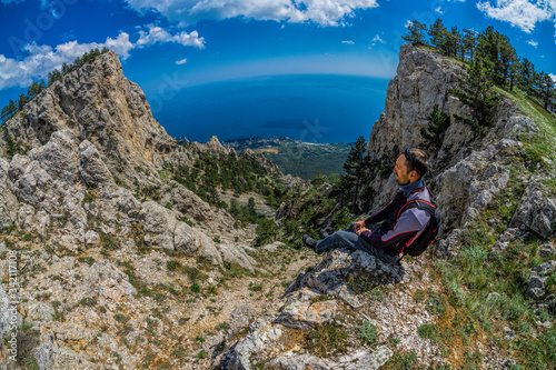 Scenic panoramic high angle view from top of Ai-Petri with a young man in front admiring the mountain view towards coastline between Yalta, Mishor and Alupka with clouds in morning sunlight, Crimea photo