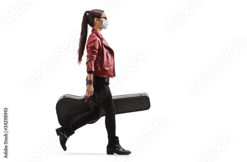 Female musician wearing a protective medical mask and walking with a guitar in a case