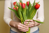 Young Woman in white top and jeans holding bouquet of tulips in her hands