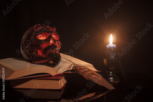 skull is lying on books near a burning candle