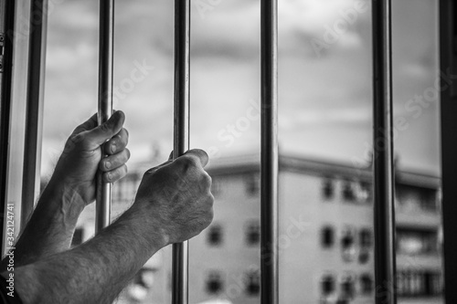 man's hands holding window bars, looking outside concept of quarantine at home by world pandemic coronavirus