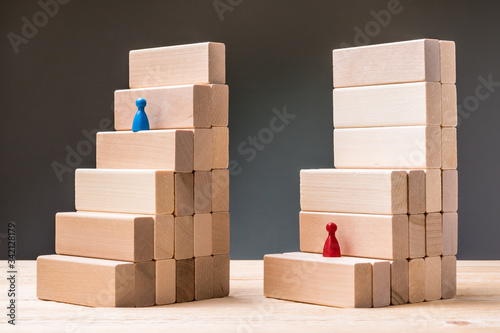 Steps made of wooden blocks. The blue pawn follows a simple and quick path. The red pawn has a difficult insurmountable barrier. Different difficulty level, injustice, concept. photo