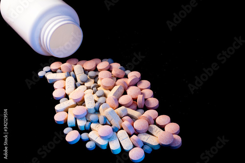 many pills that fell out of a bottle, on a black background, concept of addictions, medicines and dependency photo