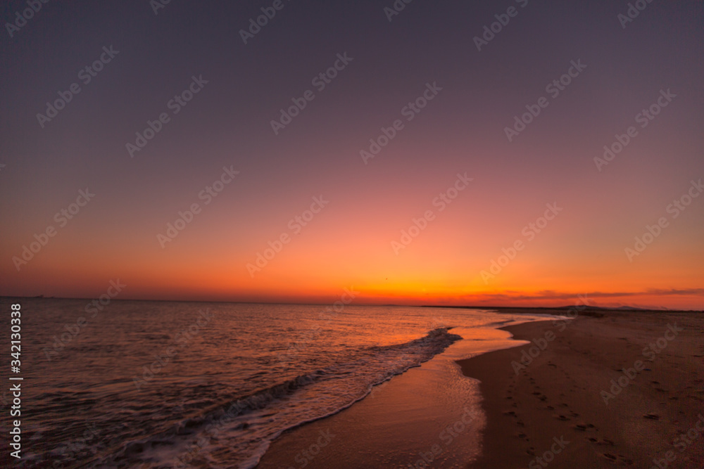 Incredibly beautiful sunset on the sea with pink and red sky, sun, and clean sand.