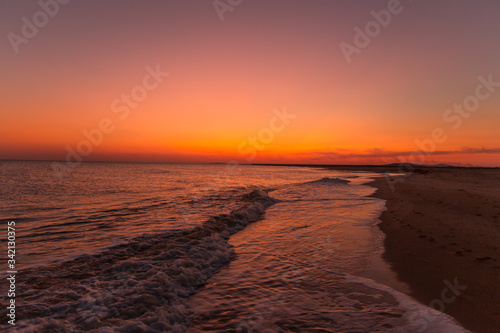 Incredibly beautiful sunset on the sea with pink and red sky, sun, and clean sand.