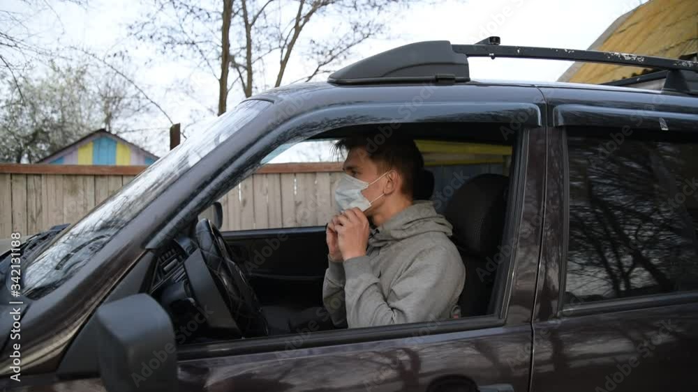 A young male driver puts on a face mask and gloves in the car.Male driver putting on medical mask and protective gloves in car before driving. A young male driver puts on a face mask and gloves in the car.Male driver putting on medical mask and protective gloves in car before driving.
