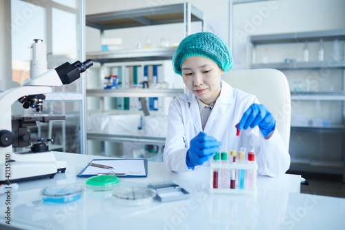 Asian nurse sitting at the table and examining the results of blood samples in the lab