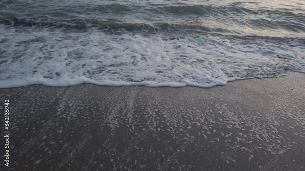 Low angle view of ocean waves crashing on the shore in bay with dark sand, a lot o foam and green emerald colored water Low angle view of ocean waves crashing on the shore in bay with dark sand, a lot o foam and green emerald colored water