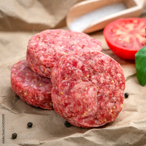 Homemade raw ground beef and Burger Patty with Basil, tomatoes and seasonings on craft paper.