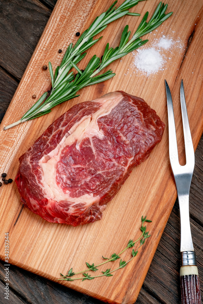 Raw rib eye steak of beef on wooden Board with rosemary and thyme on wooden background, top view