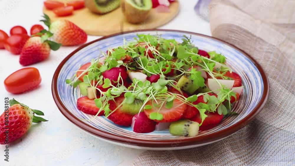 Vegetarian fruits and vegetables salad of strawberry, kiwi, tomatoes, microgreen on white concrete background and linen textile sprinkled with vinegar. Side view, close up. Vegetarian fruits and vegetables salad of strawberry, kiwi, tomatoes, microgreen on white concrete background and linen textile sprinkled with vinegar. Side view, close up.