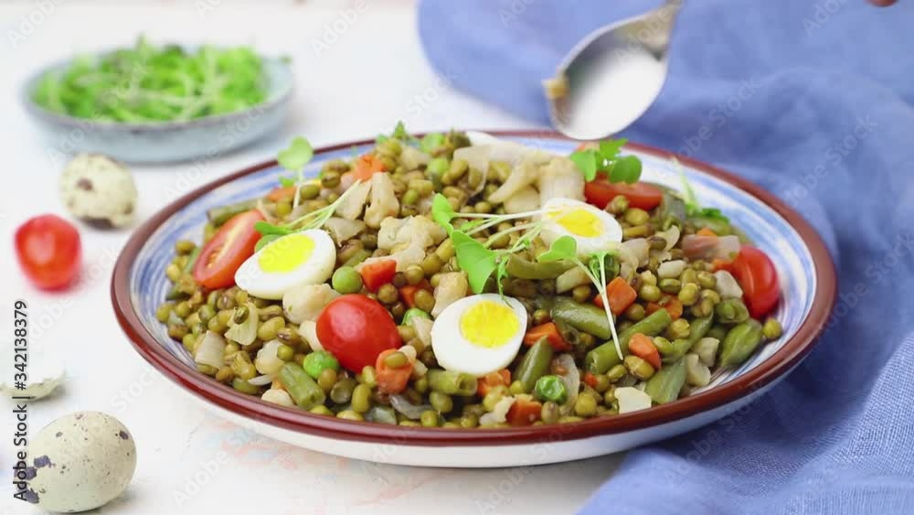 Mung bean porridge with quail eggs, tomatoes on a white concrete background and blue textile, stir with a spoon. Side view, close up.