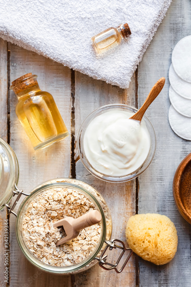 Concept of natural organic ingredients in cosmetology and gentle home treatment in quarantine. Do it yourselft. Handmade mask with oat, yogurt, oil. Wooden background. Flat lay top view close up
