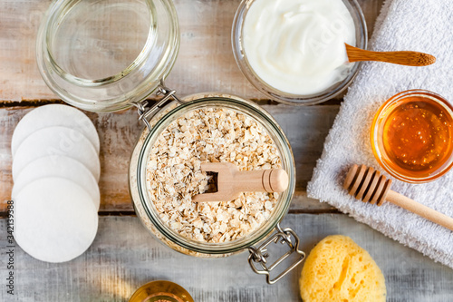 Concept of natural organic ingredients in cosmetology and gentle home treatment in quarantine. Do it yourselft. Handmade mask with oat, honey, yogurt. Wooden background. Flat lay top view close up photo