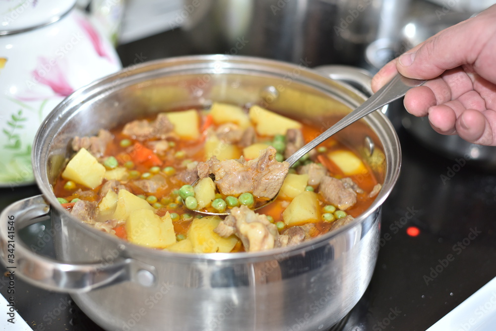 In a saucepan, cooked stew vegetables: potatoes, carrots, peas with meat. The cook takes a sample with a spoon. Healthy food that is good for the stomach. In a saucepan, cooked stew vegetables: potatoes, carrots, peas with meat. The cook takes a sample with a spoon. Healthy food that is good for the stomach.
