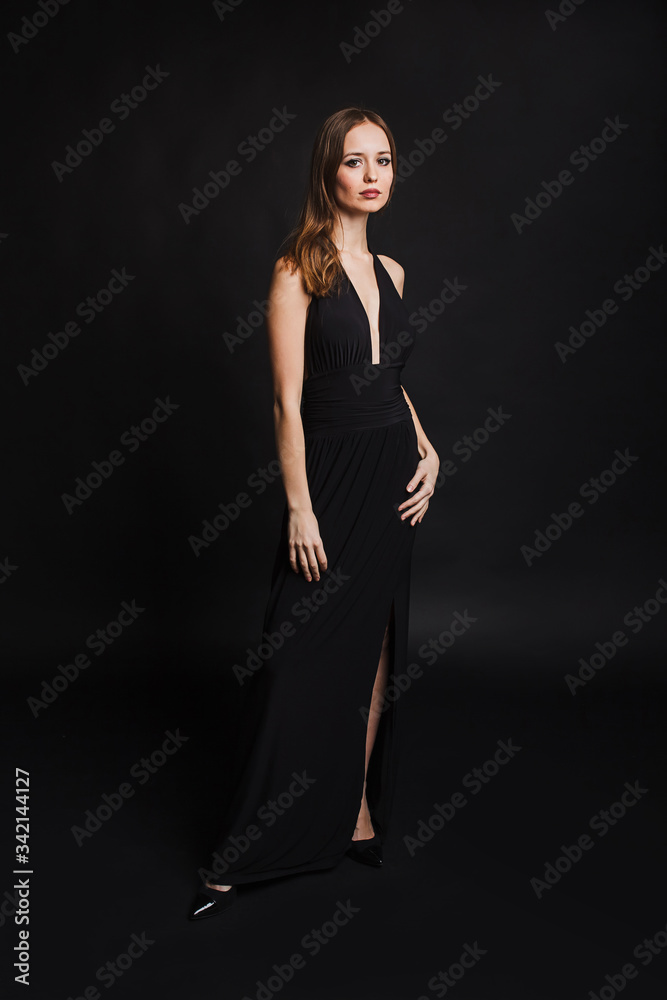 A girl with brown hair in a black long dress in the Studio on a black background. fashion photo shoot on a dark background