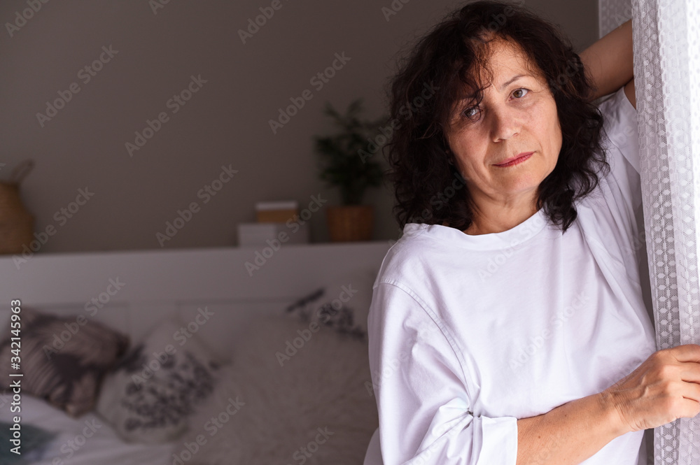 A person posing for the camera. Portrait of a woman seniors in white clothes, she stands near the window and is sad. Copy space. Soft focus A person posing for the camera. Portrait of a woman seniors in white clothes, she stands near the window and is sad. Copy space. Soft focus