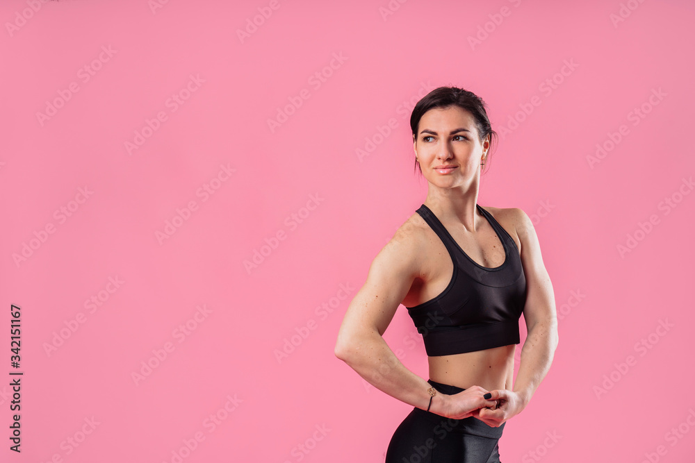 Indoor fashion portrait of a young caucasian brunette beautiful woman. Fun and cute smiling, wearing a sexy casual black sports outfit. Isolated on pink background. Hands on slim waist. Sportswoman Indoor fashion portrait of a young caucasian brunette beautiful woman. Fun and cute smiling, wearing a sexy casual black sports outfit. Isolated on pink background. Hands on slim waist. Sportswoman