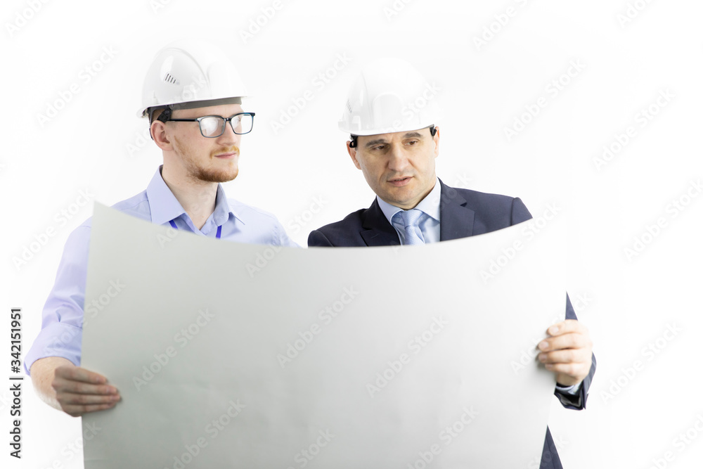 Two handsome positive construction engineers of different ages in white helmets look at drawing. boss gives instructions to subordinate and discuss details of project isolated on white background. Two handsome positive construction engineers of different ages in white helmets look at drawing. boss gives instructions to subordinate and discuss details of project isolated on white background.
